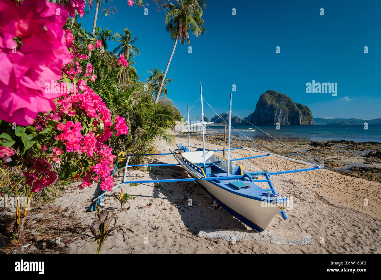 Native banca Boot und lebendigen Blumen im Las Cabanas am Strand mit erstaunlichen Pinagbuyutan Insel im Hintergrund. Exotische Natur Landschaft in El Nido, Palawan Stockfoto