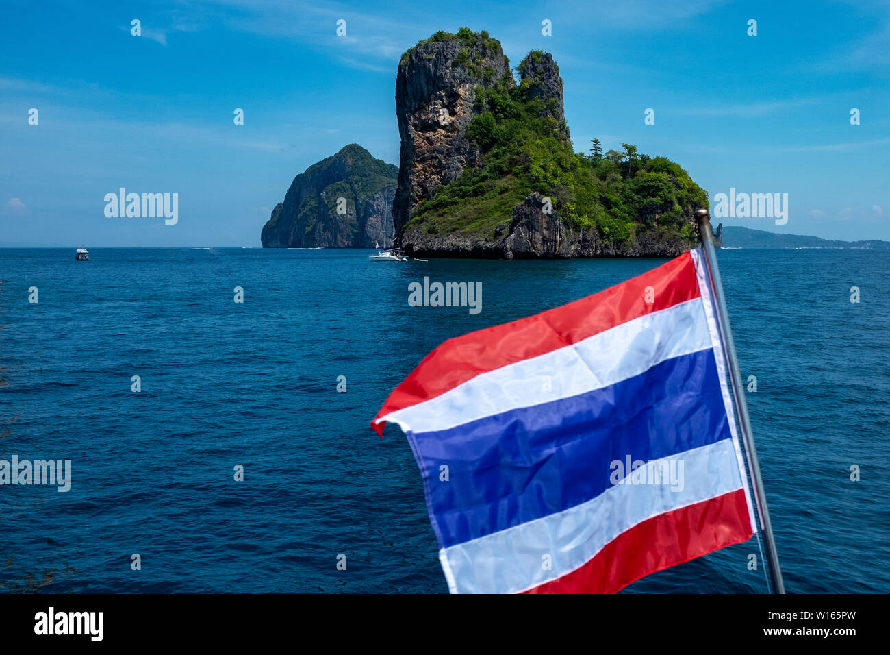 Eine Marine eines kleinen Kalkstein thailändischen Insel in das glitzernde Wasser der Andaman See, mit der Flagge von Thailand im Vordergrund flatterte. Stockfoto