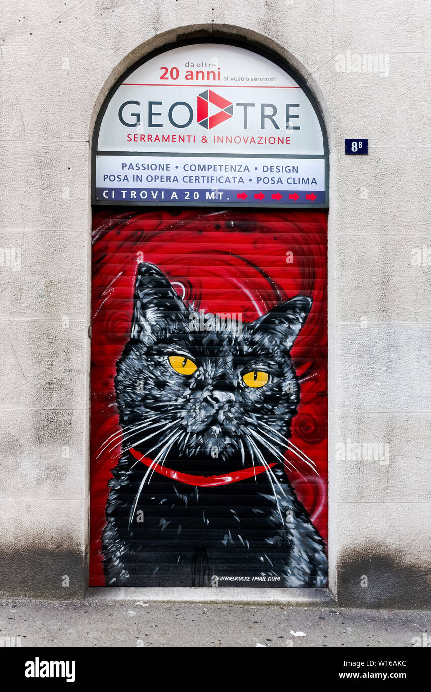 Schwarze Katze auf einem roten Hintergrund eines geschlossenen Rollladens gemalt. Shop vor einem Fenster Türen und Fensterläden zu speichern. Triest, Italien, Europa, EU. Stockfoto