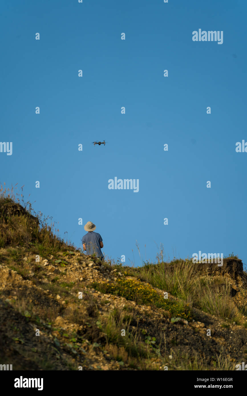 Mann auf der Klippe fliegen einer Drohne an einem Strand. Großbritannien Stockfoto