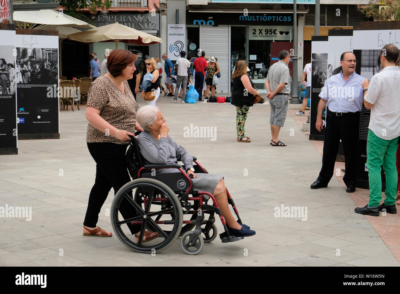 Ältere Frau im Rollstuhl mit einem Hausmeister ihn von hinten in einer Plaza in Granada, Spanien; für einen Spaziergang. Stockfoto