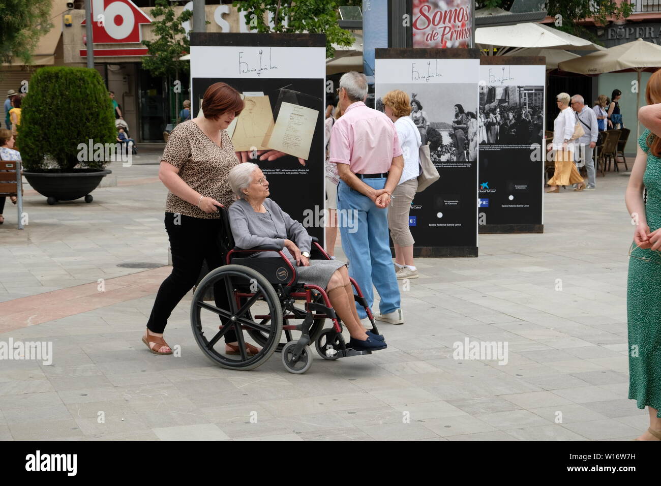 Ältere Frau im Rollstuhl mit einem Hausmeister ihn von hinten in einer Plaza in Granada, Spanien; für einen Spaziergang. Stockfoto