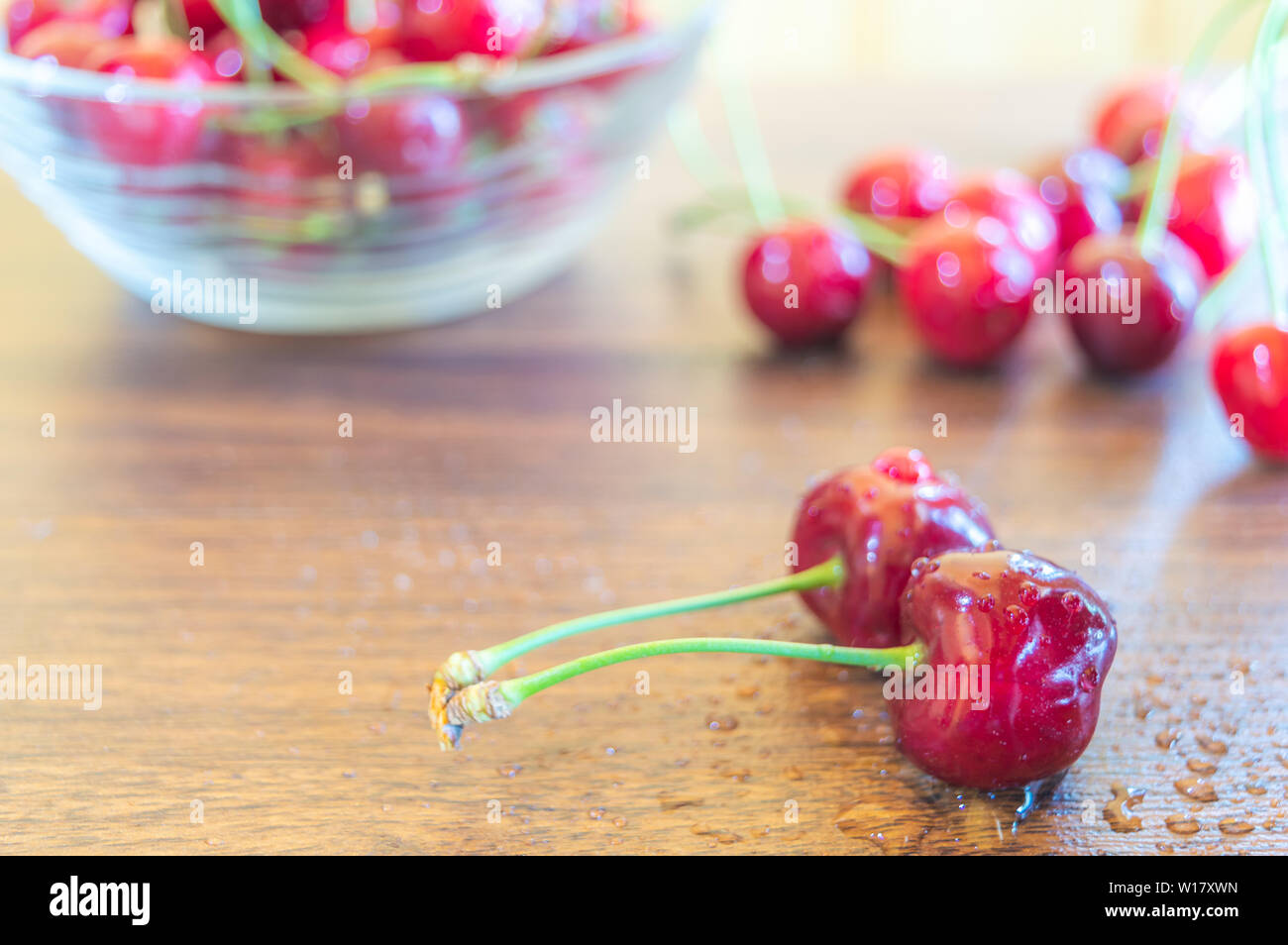 Rote reife Kirschen in einem Glas Schüssel gehalten auf einem Holztisch in der Küche. Wasser besprengt wurden frische Kirschen auf dem hölzernen Tisch gehalten. Stockfoto