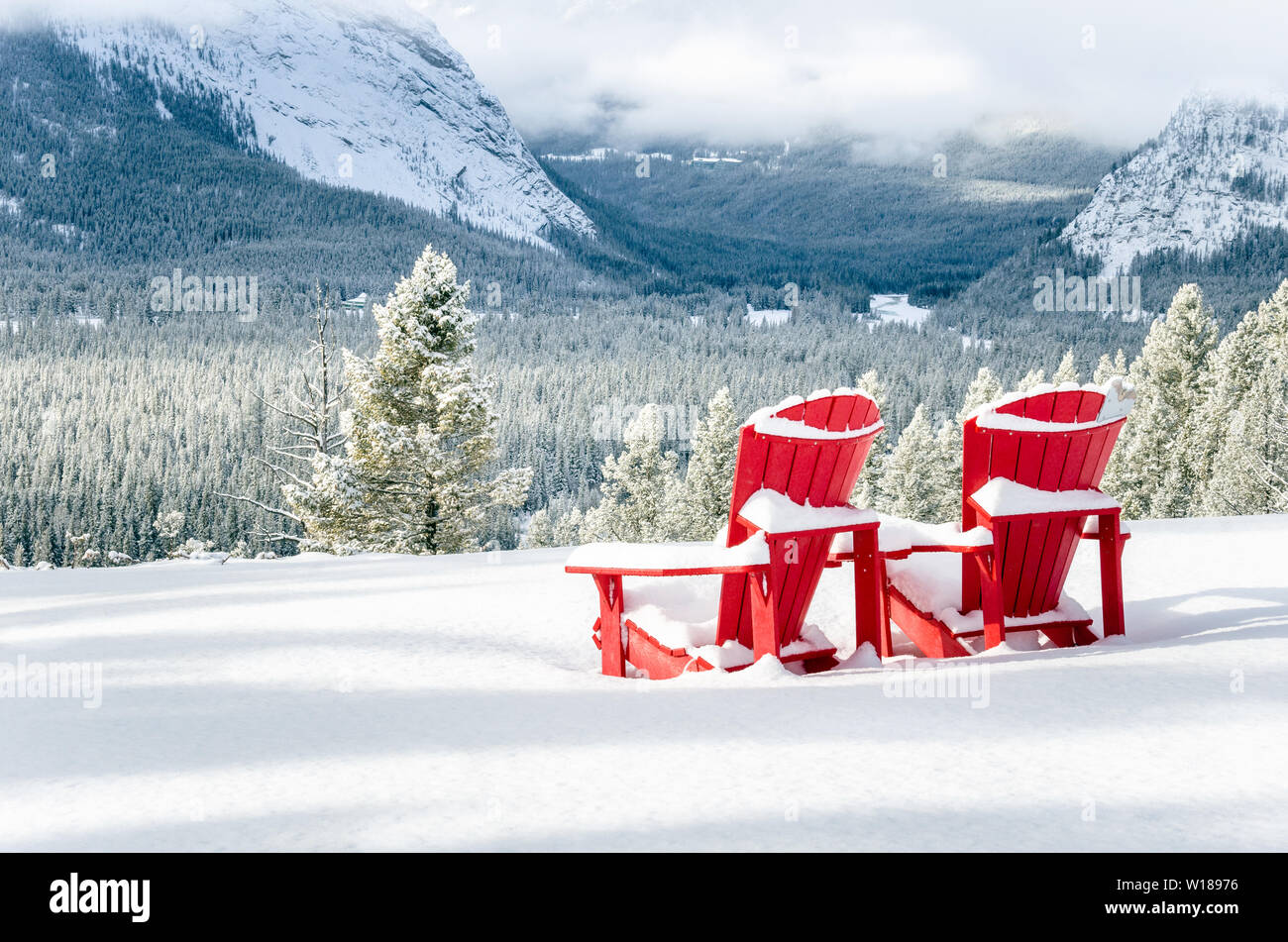 Schnee Rot Adirondack Stühle mit Blick auf eine gefrorene bewaldetes Tal an einem Wintertag. Banff National Park, AB, Kanada. Stockfoto