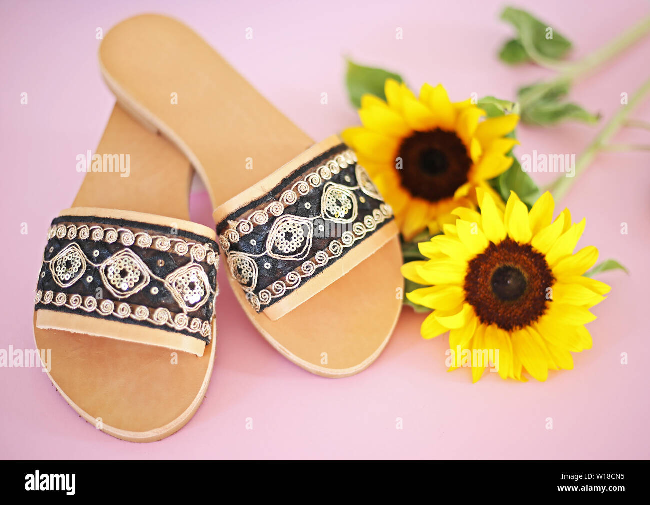 Griechische Sandalen aus Leder mit goldenen Details - rosa Hintergrund -  Sonnenblumen Dekor - Frau Schuhe Werbung Stockfotografie - Alamy