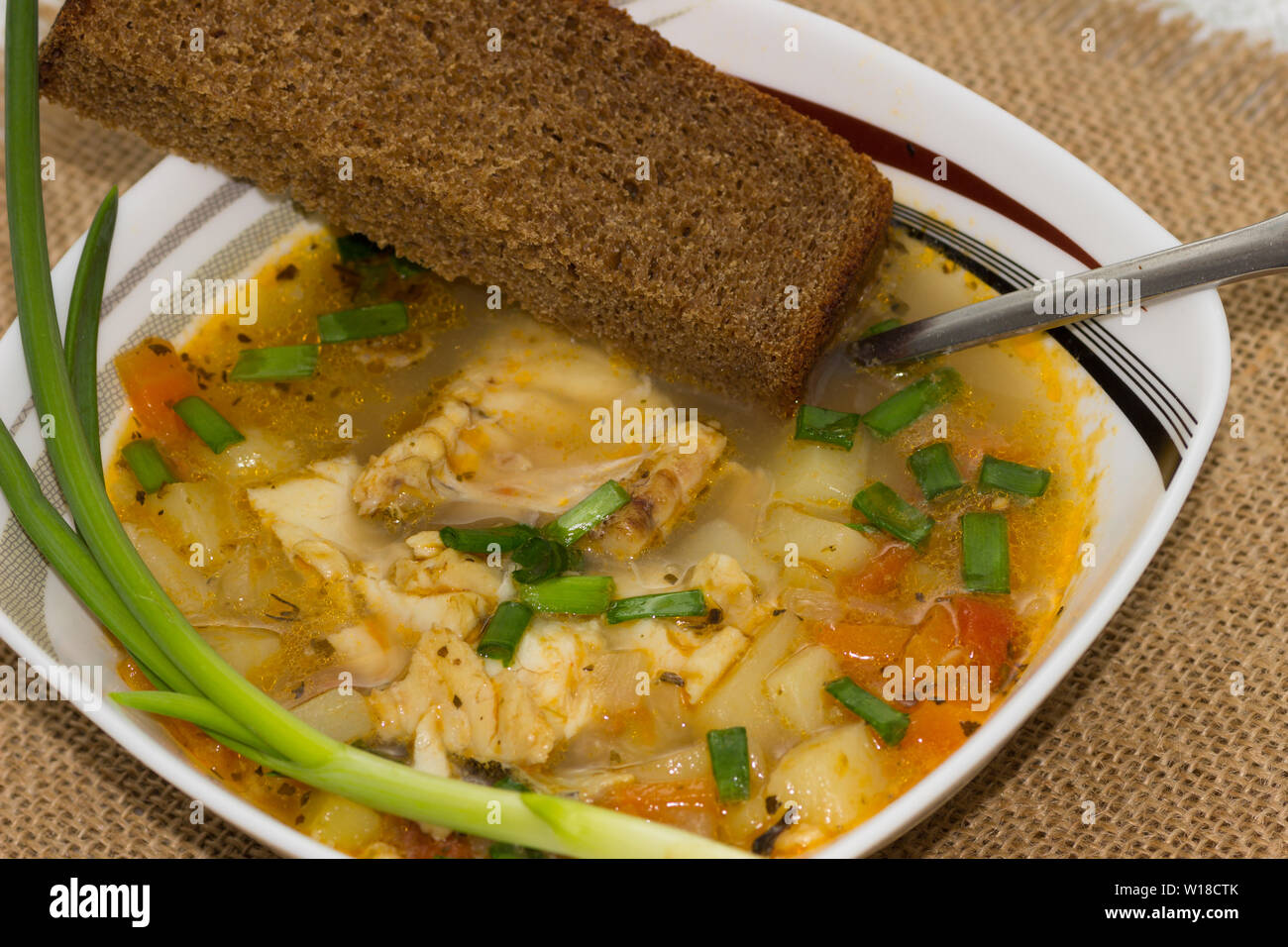 Schüssel von Kabeljau, Tomaten und grüne Zwiebel Suppe mit einem Stück Roggenbrot auf eine Serviette Stockfoto