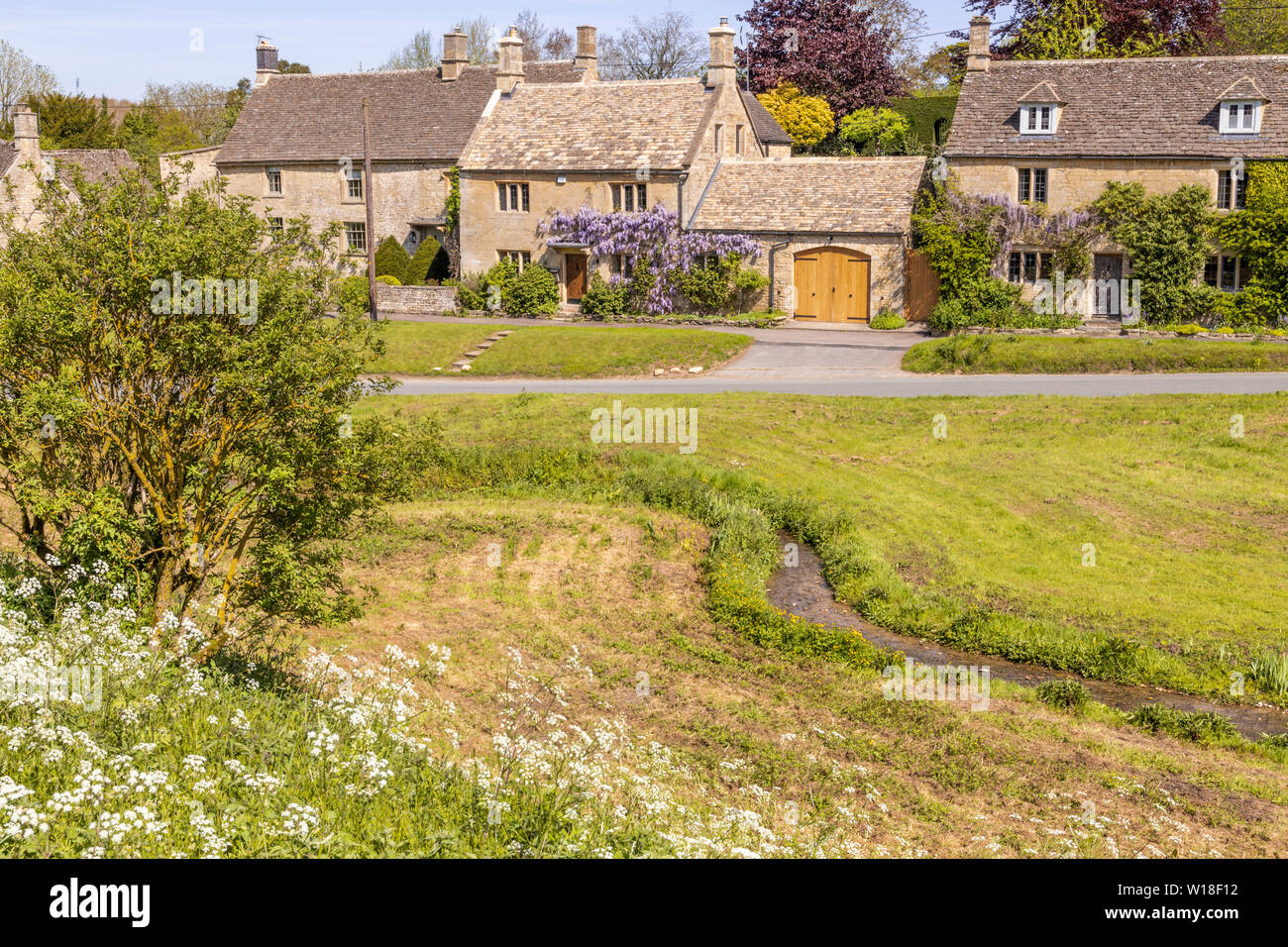 Ein Strom fließt durch das Grün im Cotswold Dorf Little Barrington, Gloucestershire, Großbritannien Stockfoto