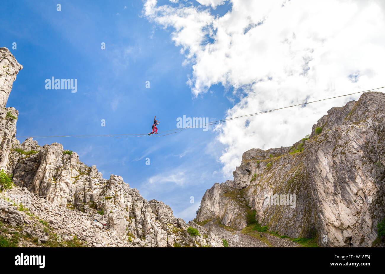 Junger Mann auf einem Highline oben scharf gezackten Klippen. Slackline in den Bergen mit wunderschönen grünen Hänge und flauschige Wolken im Hintergrund Stockfoto