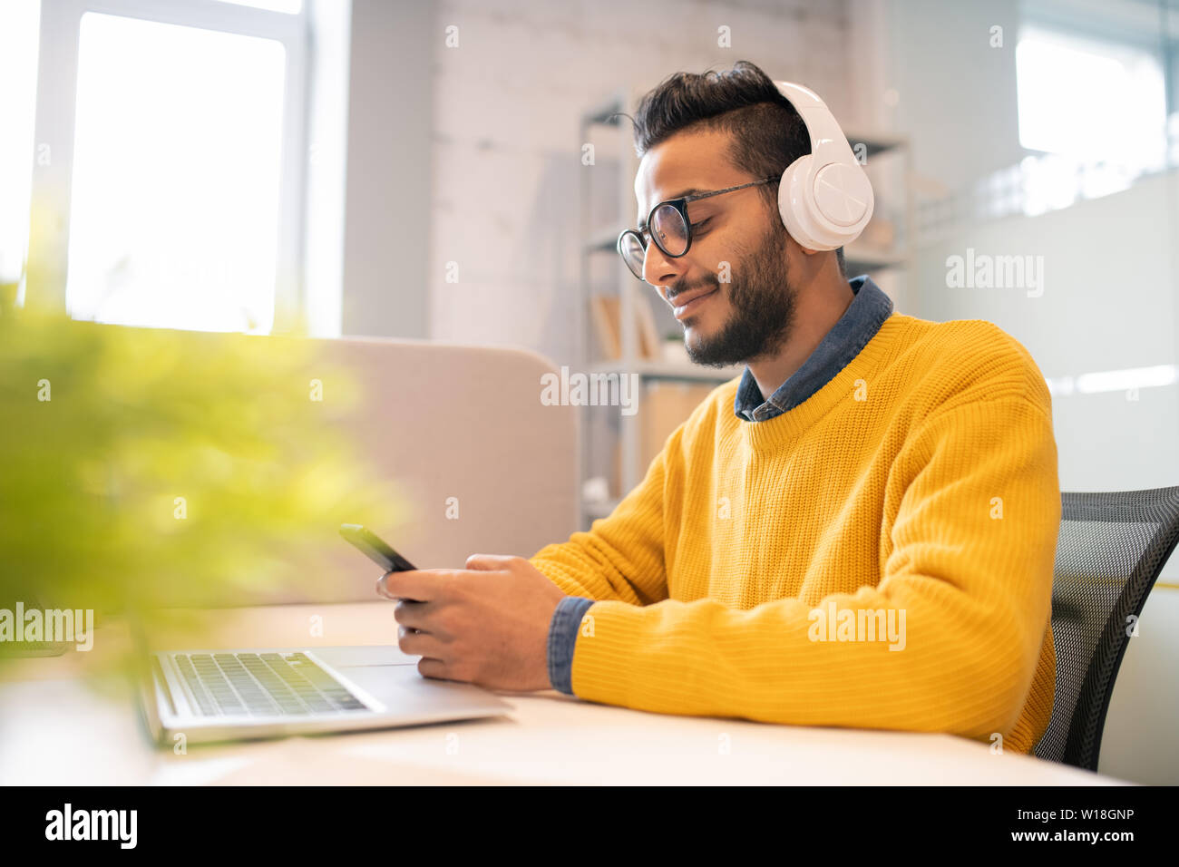 Zufrieden jungen arabischen Mann mit Bart sitzt in modernen Büro- und Messaging im Smartphone während im Büro arbeiten Stockfoto
