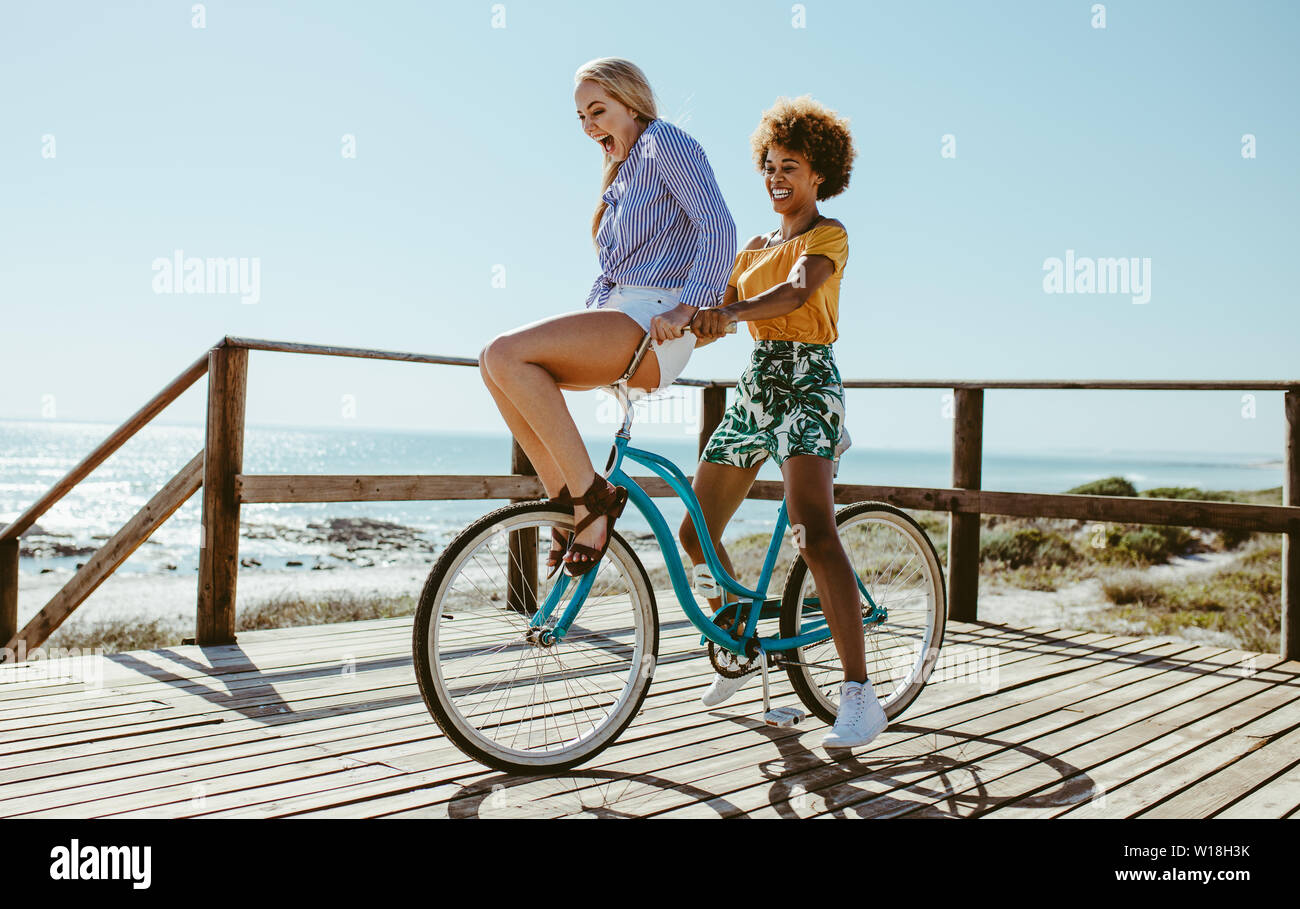 Junge Frau auf dem Lenker eines Fahrrades, geritten von ihrem Freund an einem Sommertag am Strand. Freunde gehen auf eine Fahrt mit dem Fahrrad an den Strand. Stockfoto