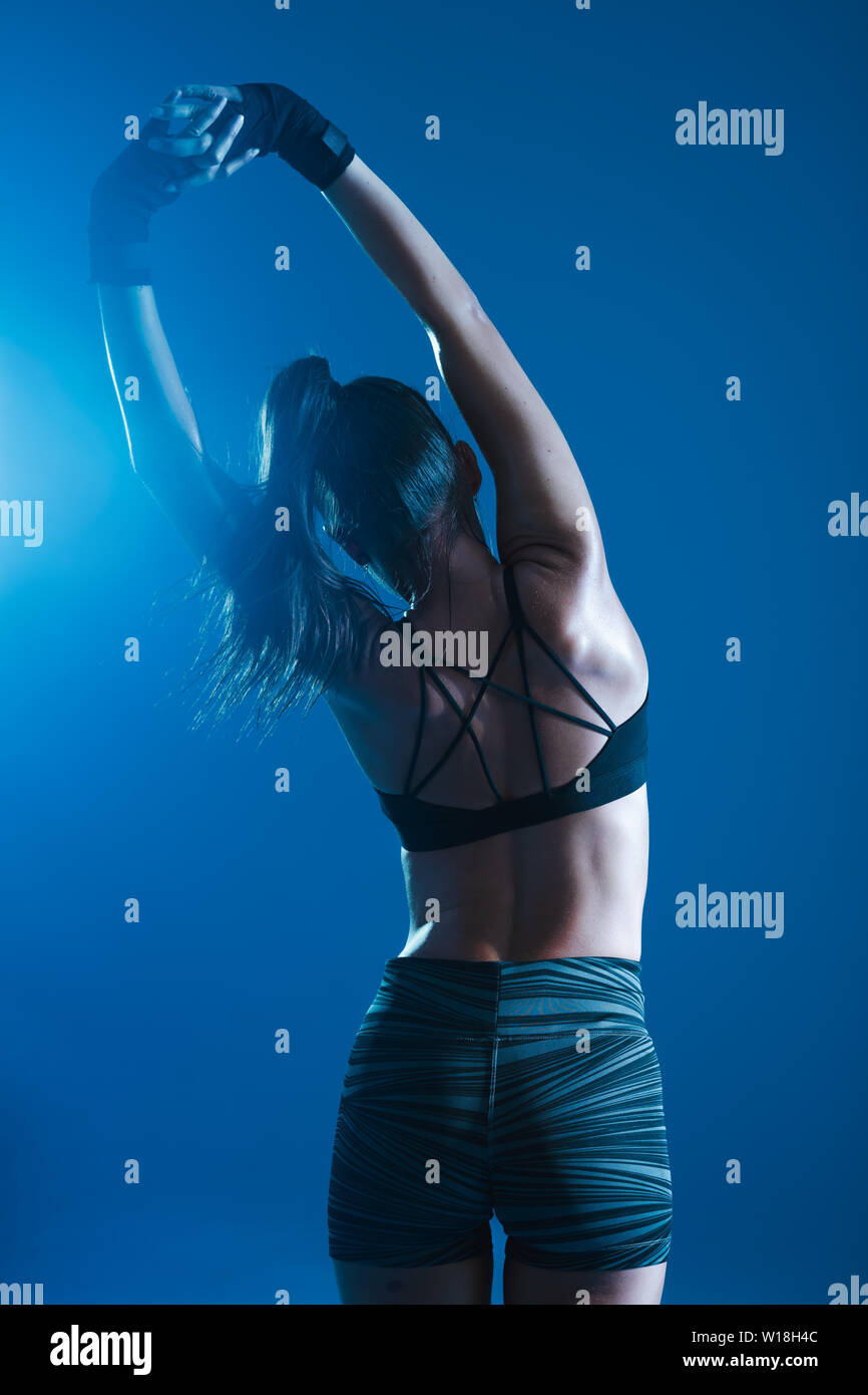 Ansicht der Rückseite des weiblichen Stretching vor blauem Hintergrund. Frau in Sportbekleidung Aufwärmen vor Training. Stockfoto