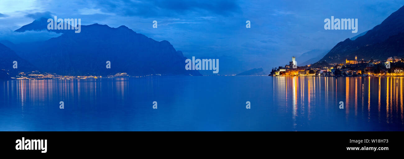 Gardasee am Abend: Auf der rechten Seite die Lichter von Limone und auf der linken Seite der Stadt Malcesine mit der mittelalterlichen Burg. Venetien, Italien. Stockfoto