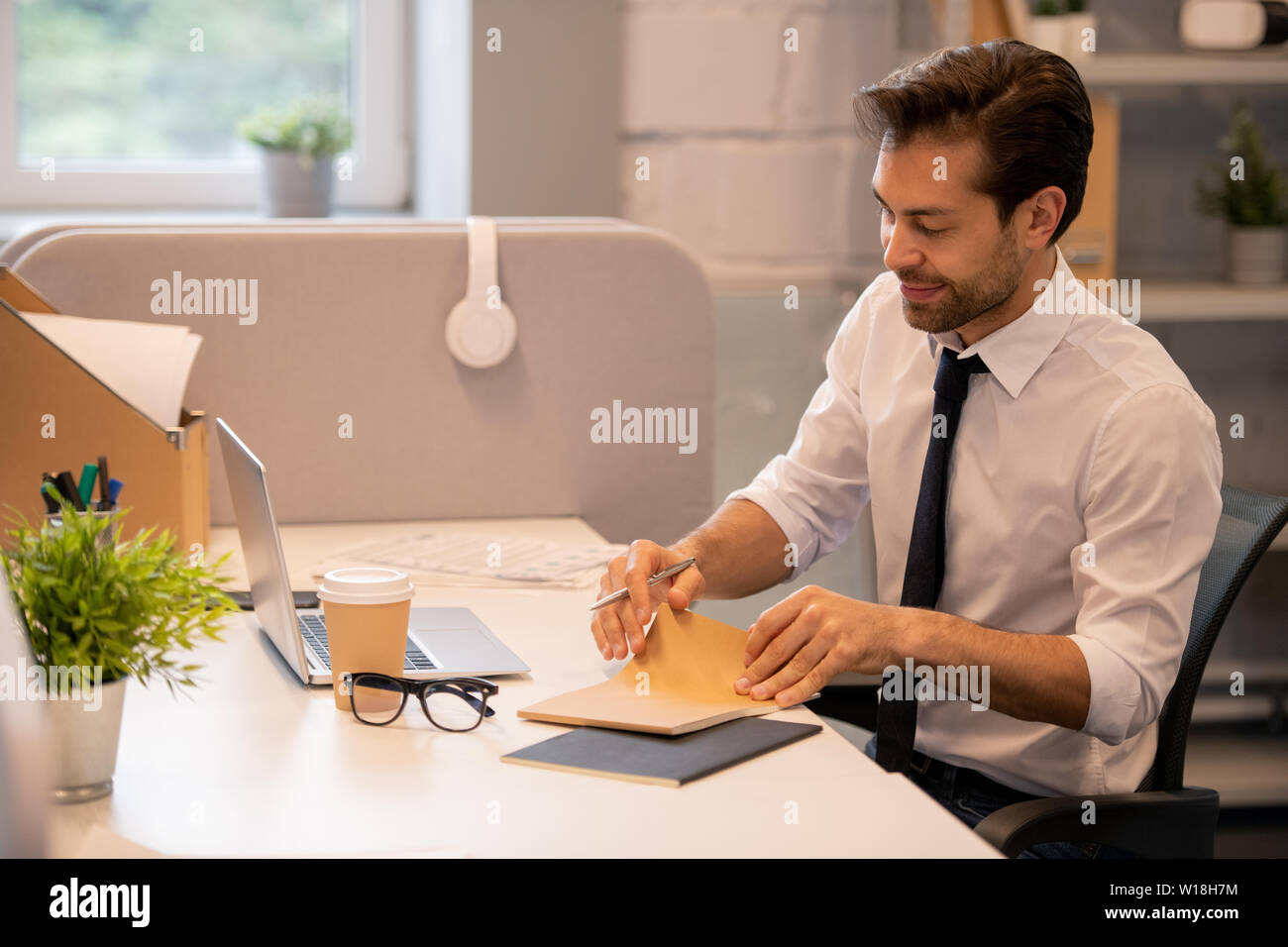 Inhalt hübscher junger white-collar-Mann am Schreibtisch in modernen Büro sitzen und Öffnen von Notepad während der Planung Ziele und Aufgaben Stockfoto