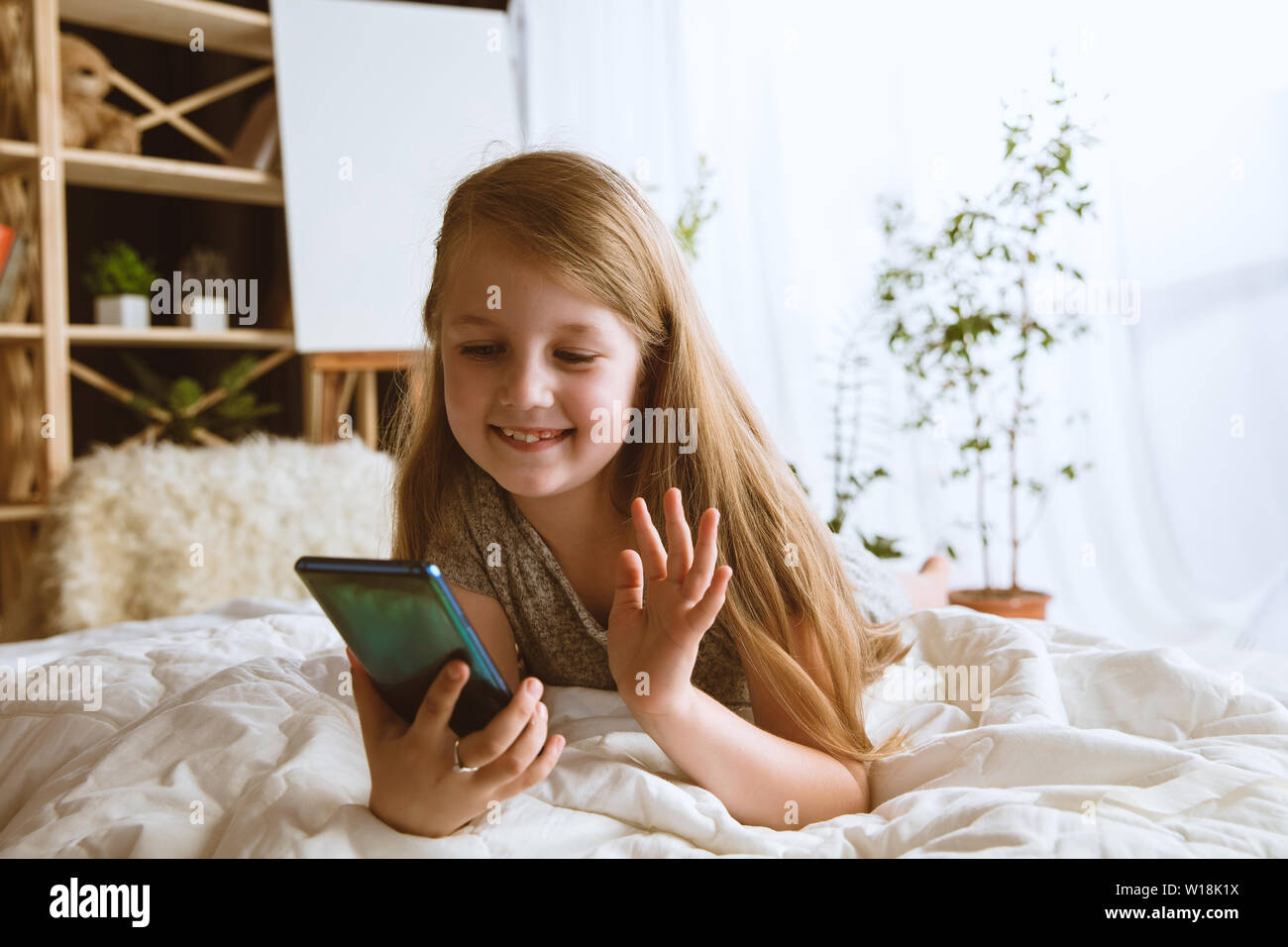 Mädchen über verschiedene Geräte zu Hause. Kleines Modell in Ihrem Zimmer mit Smartphone sitzen und selfie oder über Videochat mit ihren Freunden. Konzept der Interaktion von Kindern und moderne Technologien. Stockfoto