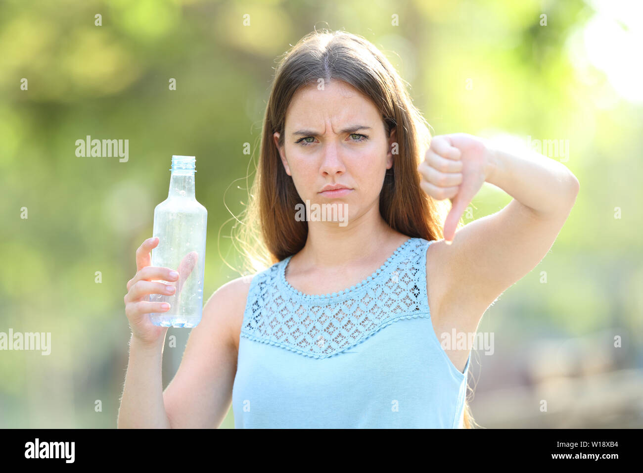Wütende Frau Holding eine Plastikflasche mit thums in einem Park mit grünem Hintergrund Stockfoto
