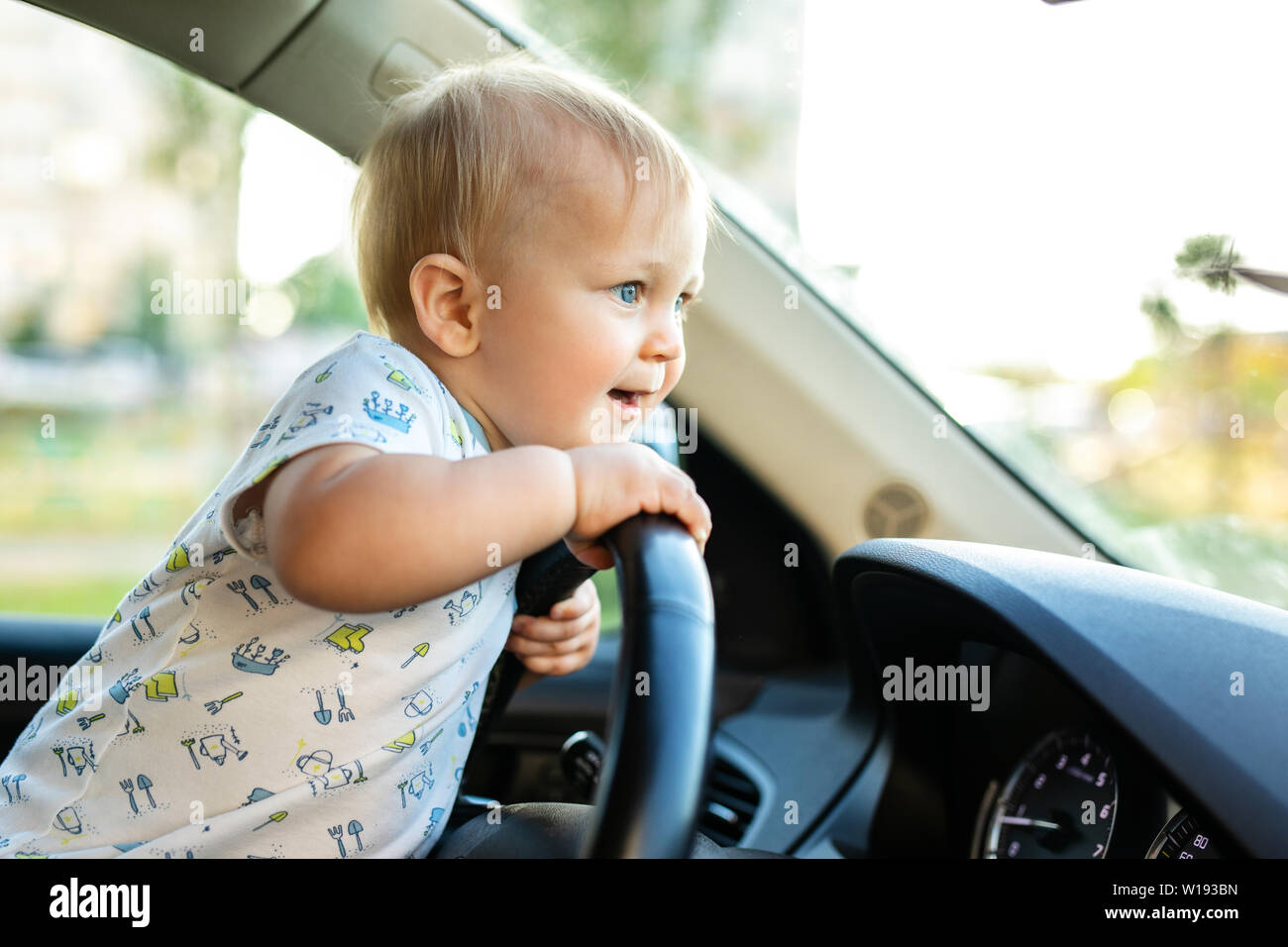 Süße kleine baby boy Fahren großes Auto, Lenkrad, lächelnd und