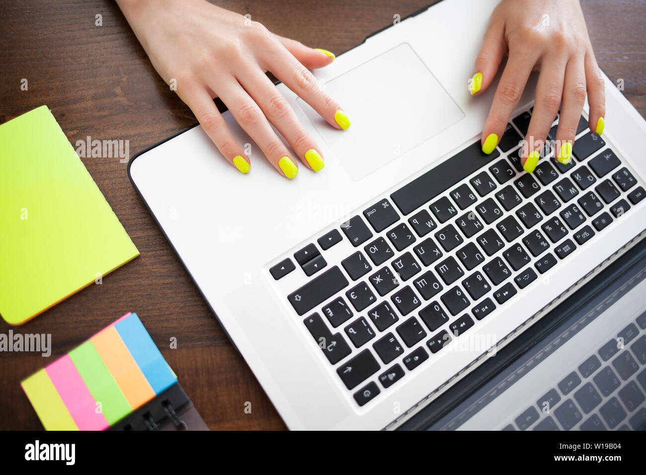 Frauenhände mit Trend gelb Maniküre Eingeben von Text auf einem Laptop Tastatur. Papier zum Schreiben. Business Planung Konzept. Stockfoto