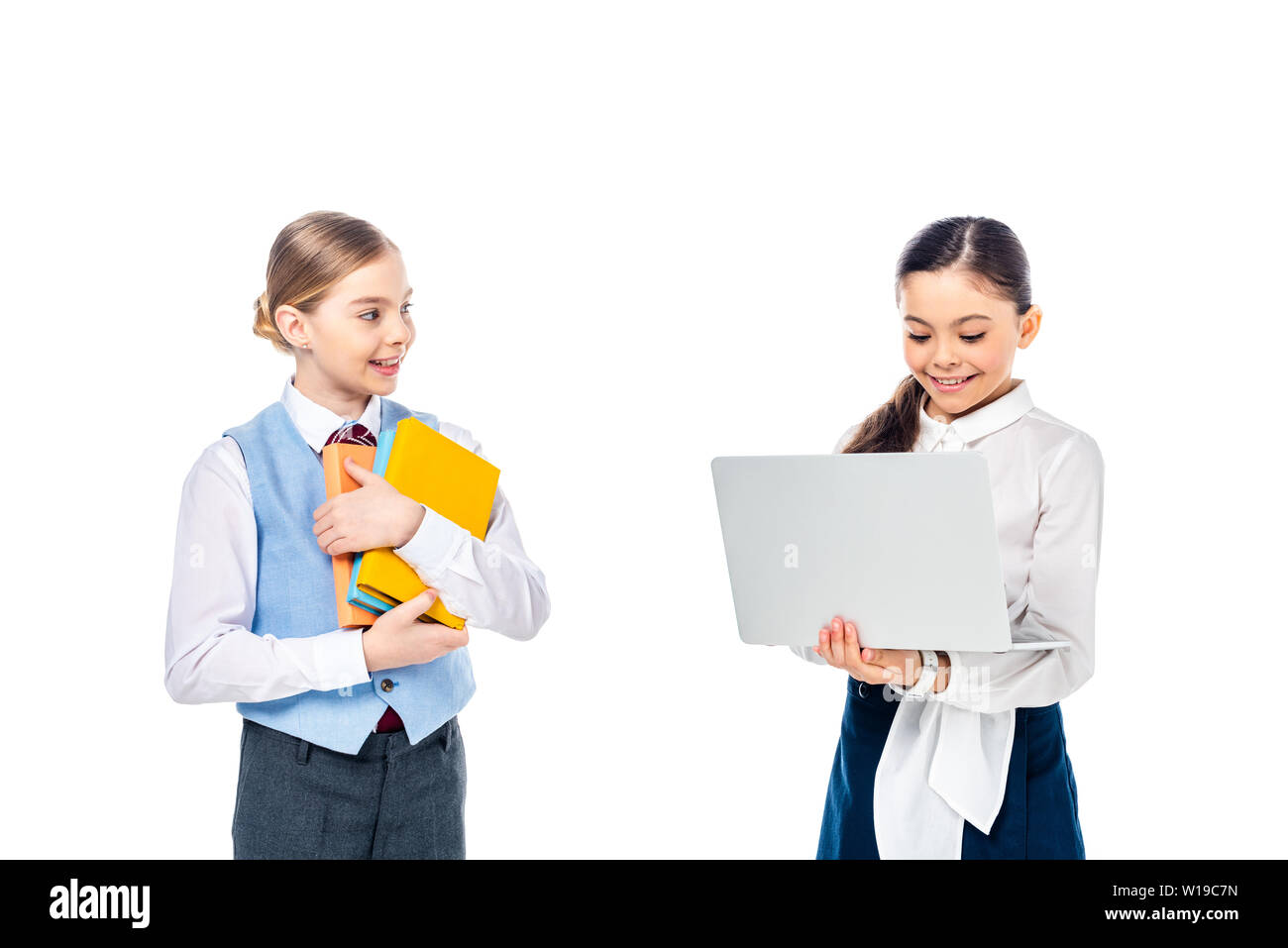 Lächelnd Schulkinder in formale Abnutzung mit Laptop und halten Bücher isoliert auf weißem Stockfoto