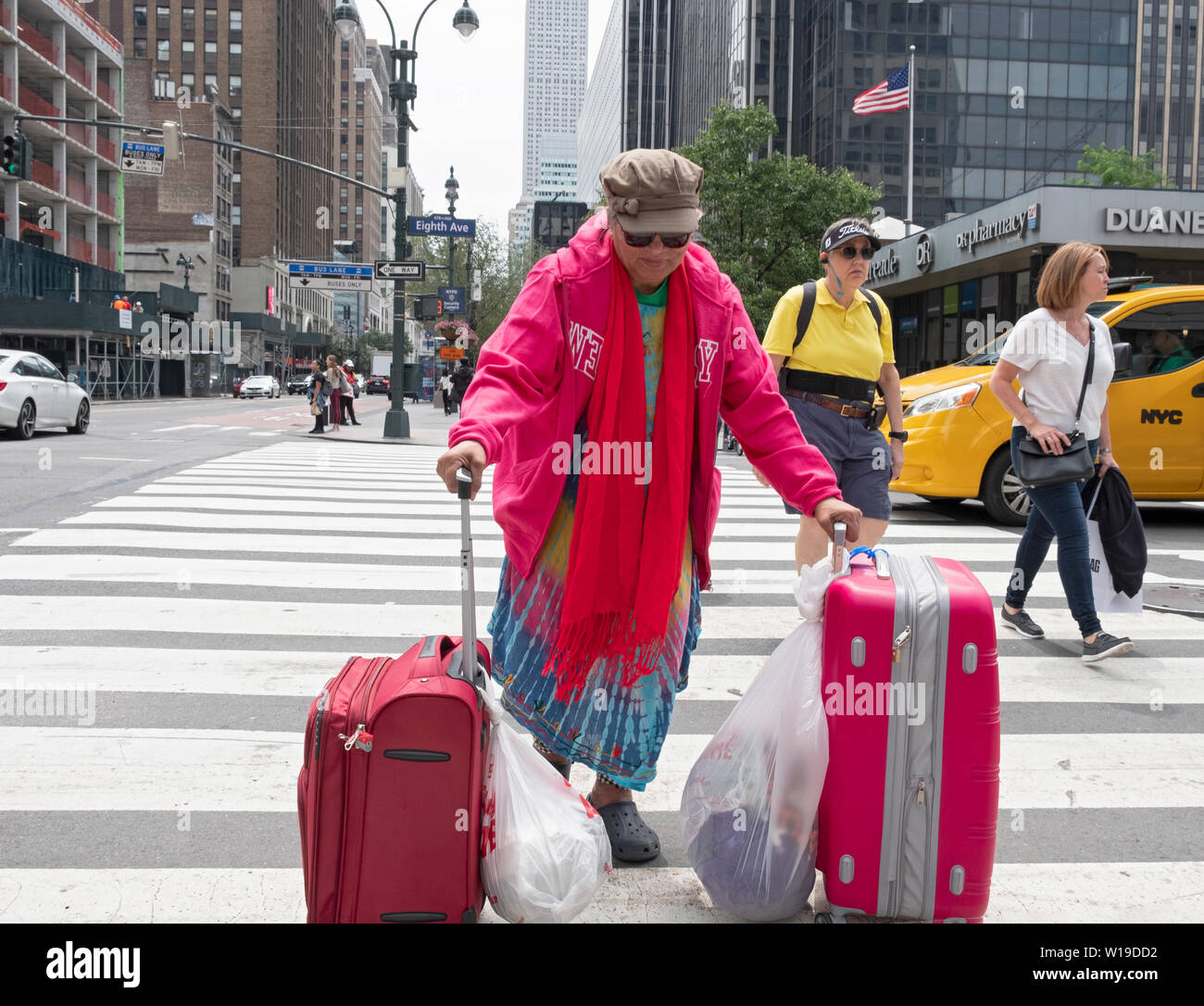 Eine ältere asiatische Frau in rosa Kreuze 8. Avenue an der 34. Straße mit passendem Gepäck. In Manhattan, New York City. Stockfoto