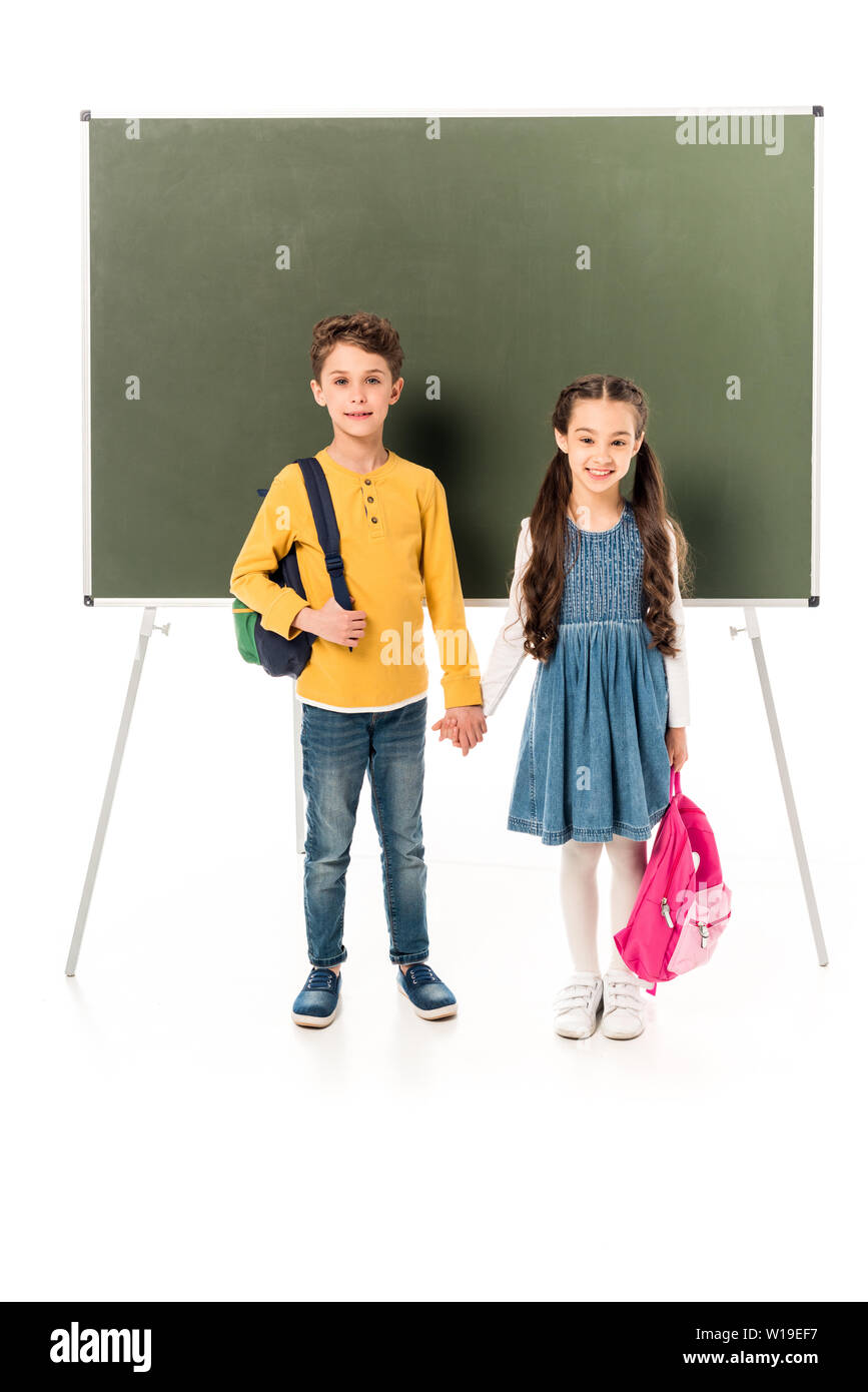 Die volle Länge der beiden Schüler mit Rucksäcken, Hände halten in der Nähe der Tafel isoliert auf weißem Stockfoto