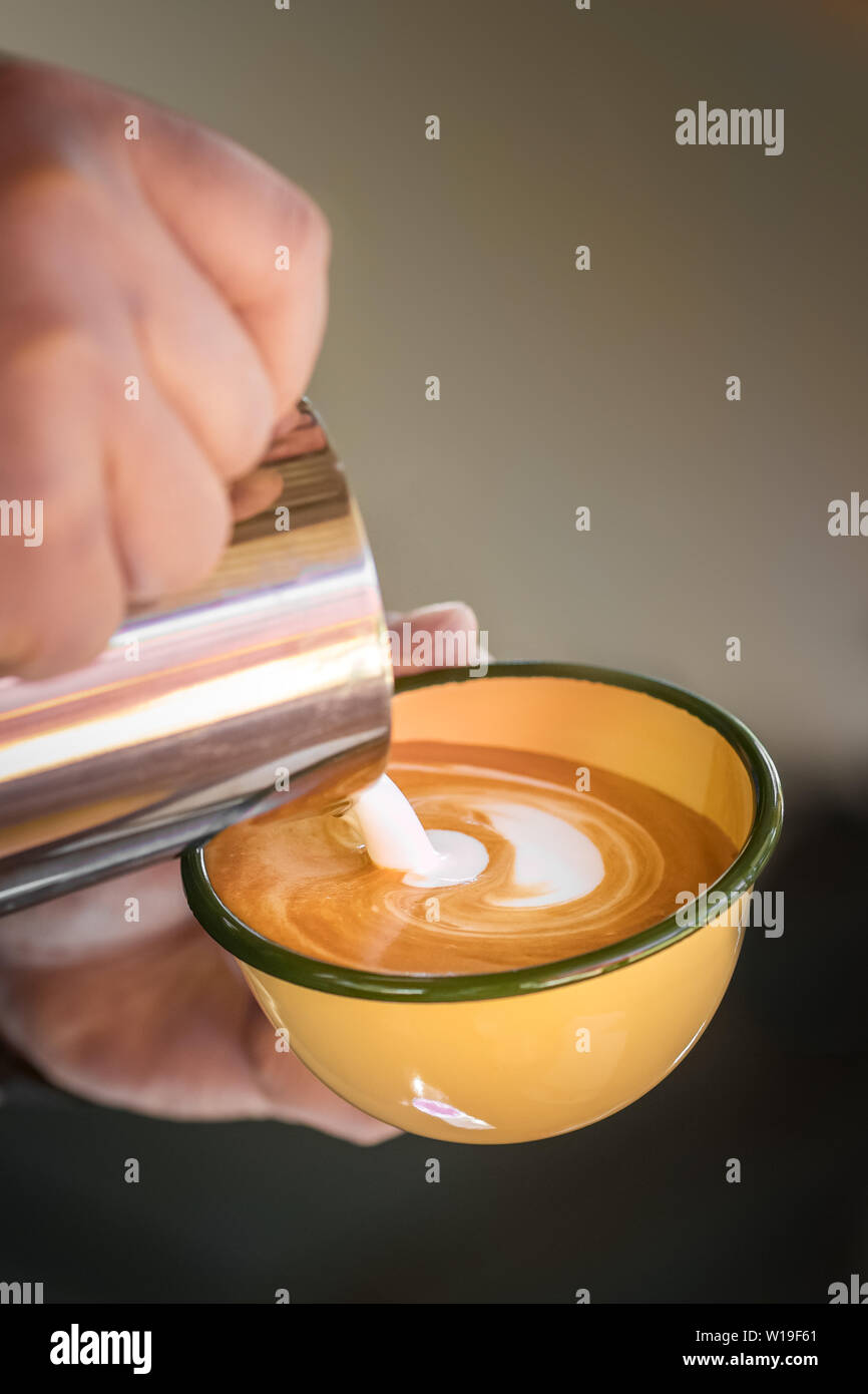 Hände von Barista, Cappuccino gießen Milch auf Espresso. Stockfoto