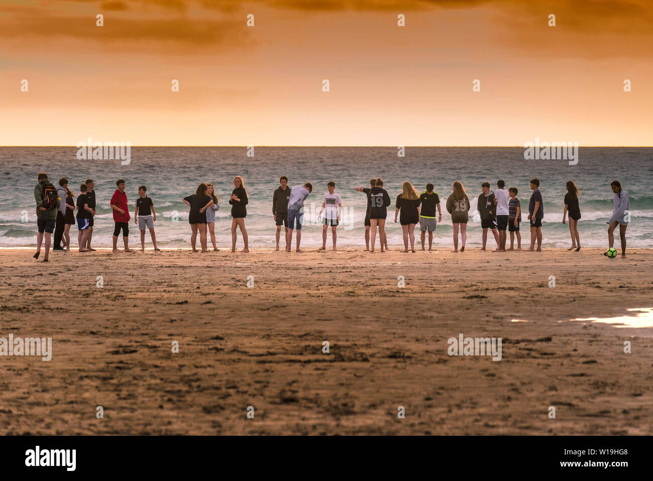Eine Gruppe von Jugendlichen heraus hängen auf den Fistral Beach in einer dramatischen Sonnenuntergang in Newquay in Cornwall. Stockfoto