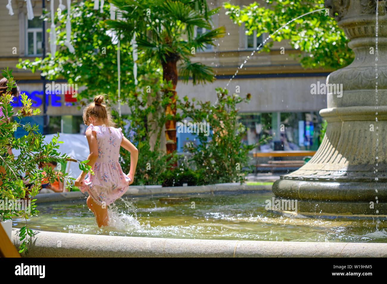 Junge Mädchen in einem Sun dress Spielen im Park Brunnen. Überspringen im kniehohen Wasser, ihre Sonne Kleid an heißen, sonnigen Tag Holding in Zagreb Stockfoto