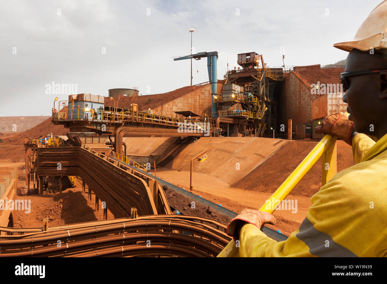 Bergbau für das Transportieren und Verwalten von Eisenerz. Vorbrecher mit Stückerz auf Transportband an Stapler und Bediener beaufsichtigt den Betrieb Stockfoto