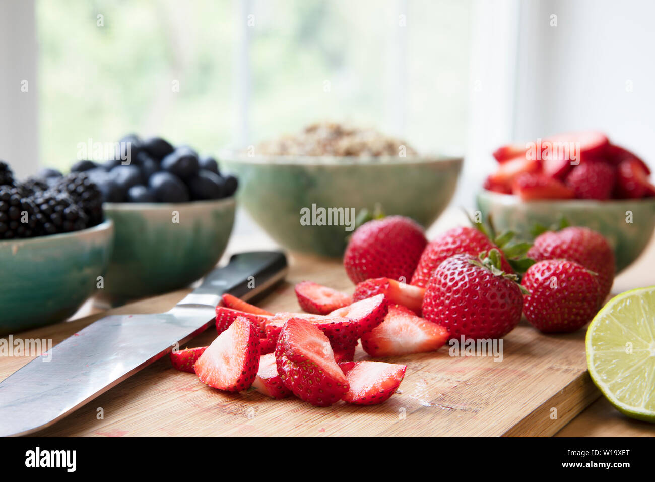 In Scheiben geschnitten und ganze Erdbeeren auf Schneidebrett mit Messer, horizontale Ausrichtung. Stockfoto