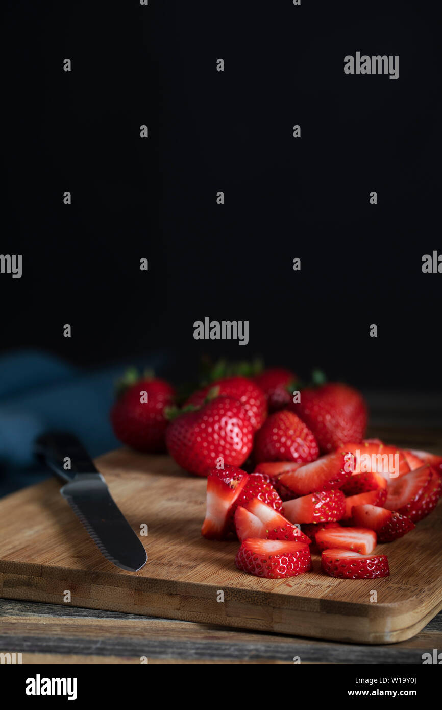 In Scheiben geschnitten und ganze Erdbeeren auf Schneidebrett mit Messer, Low Key lighitng und vertikaler Ausrichtung. Stockfoto