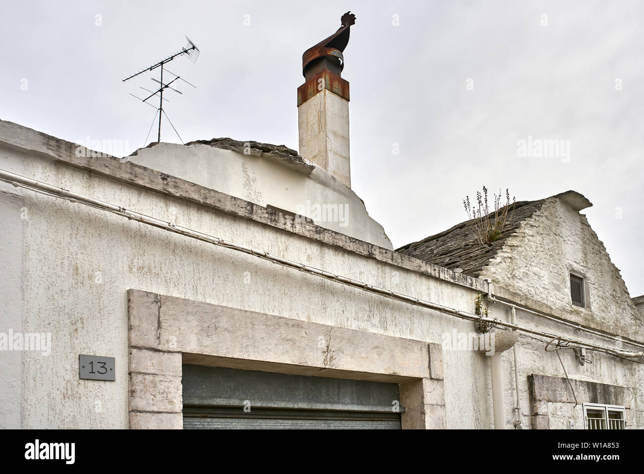 Top Teil eines alten Haus mit einer alten Kamin und eine TV-Antenne auf dem Himmel Hintergrund in Alberobello Stadt in Italien. Closeup horizontale Foto. Stockfoto