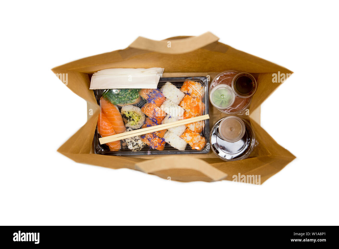 Sushi Konzept zu gehen. Blick von oben auf die Kästchen mit Sushi zum Mitnehmen Brötchen und verschiedene Sauce Cups in der braunen Papiertüte. Auf weißen, Studio shot isoliert. Stockfoto