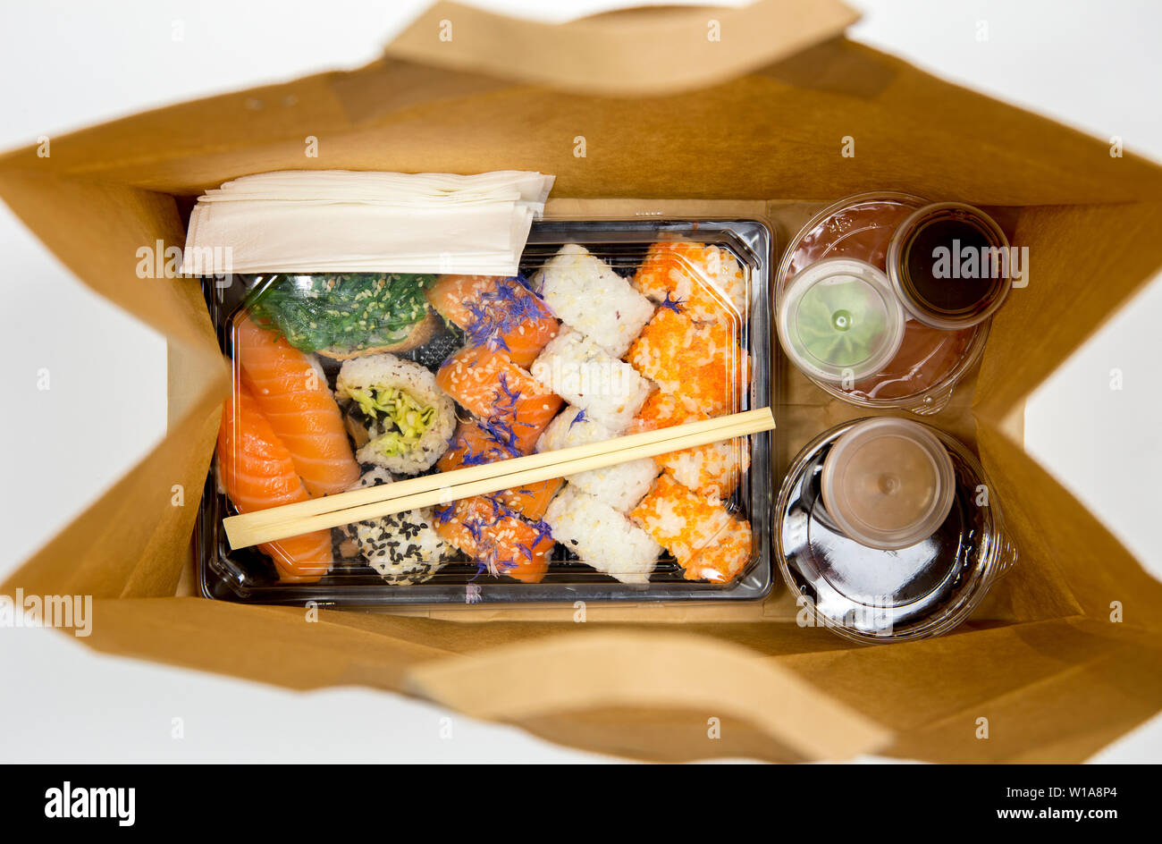 Sushi Konzept zu gehen. Blick von oben auf die Kästchen mit Sushi zum Mitnehmen Brötchen und verschiedene Sauce Cups in der braunen Papiertüte. Auf weißen, Studio shot isoliert. Stockfoto