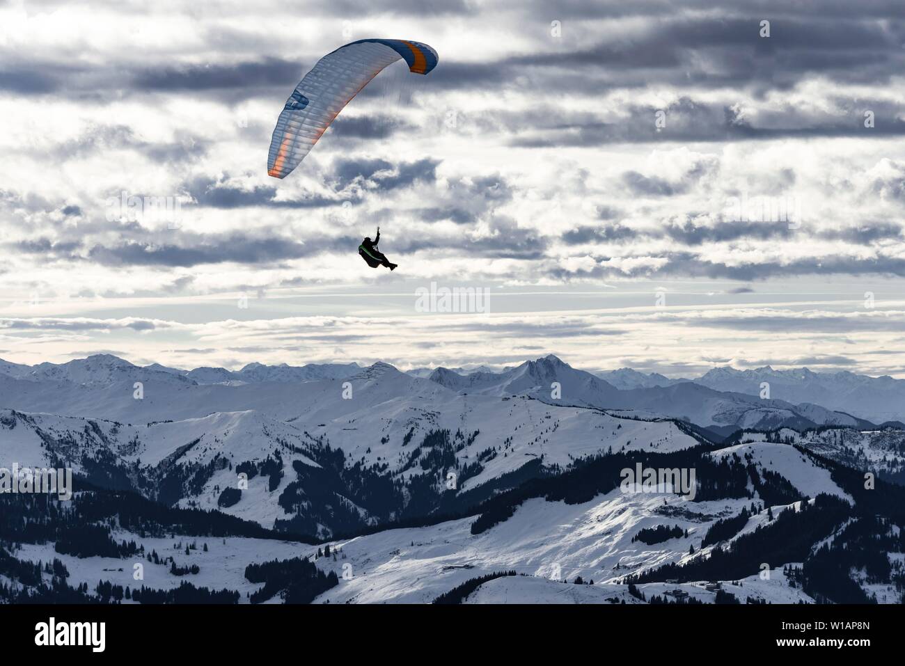 Paragliding in der Luft vor einer verschneiten Alpenkamm im Winter, Brixen im Thale, Tirol, Österreich Stockfoto