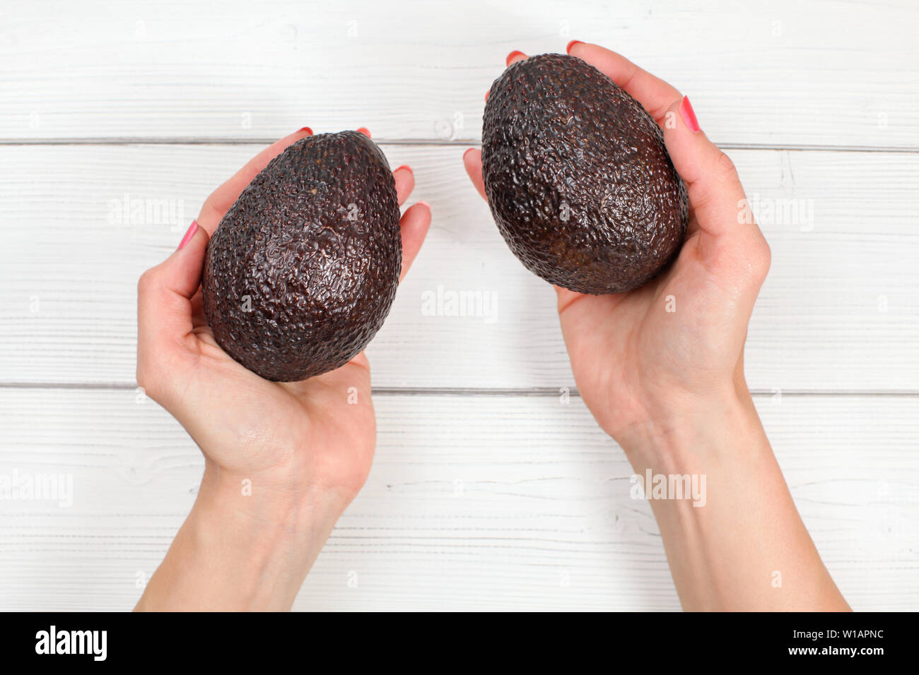 Auf frau Hände halten zwei reife Braue avocados über White boards Schreibtisch. Stockfoto