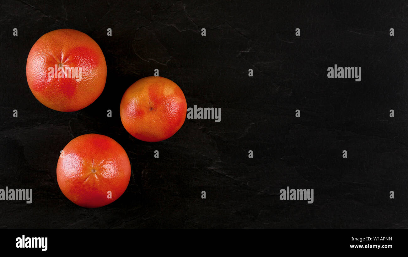 Von oben nach unten anzeigen, drei rosa Grapefruits auf schwarzem Marmor, Banner mit Platz für Text auf der rechten Seite. Stockfoto