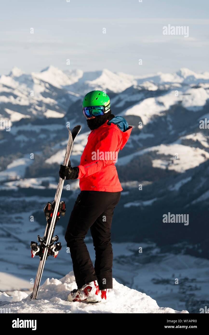 Weibliche Skifahrer mit Ski Helm mit Ski auf der Piste über dem Tal, in die Kamera schaut, hinter den Bergen, SkiWelt Wilder Kaiser Stockfoto