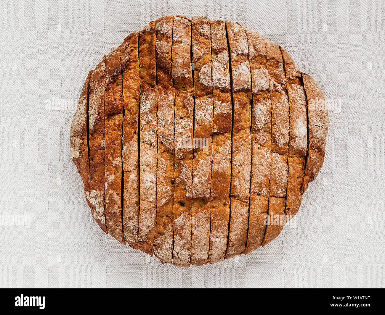 In Scheiben geschnitten runden Laib Schwarzbrot mit einem leckeren knusprig braune Kruste auf ein graues Leinen Tischdecke. Lecker, nützlich und nahrhaft. Direkt oben betrachten. Stockfoto