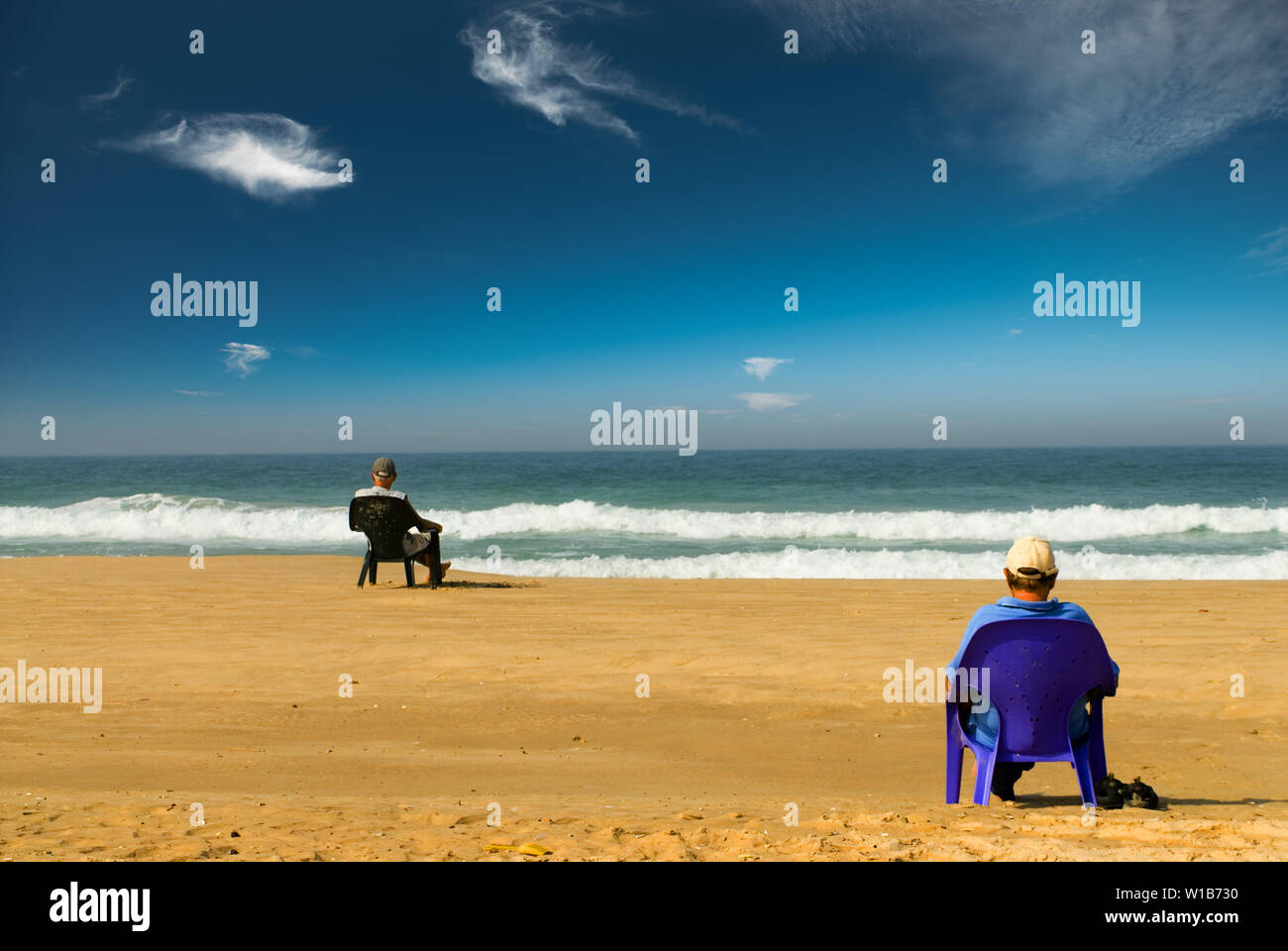 Zwei Mann mit Blick auf das Meer sitzen auf einem Sandstrand auf Plastikstühlen. Anzeigen lesen Stockfoto