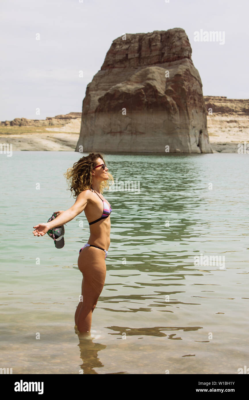 Einen mittleren Alters touristische Frau im Bikini in der Sonne und Wasser in Lone Rock Beach, Lake Powell, Big Water, Utah, USA Stockfoto