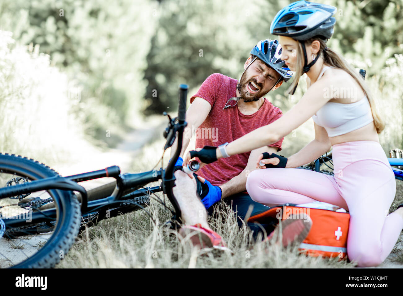 Frau Leistung erster Hilfe zu einem Mann mit Knieverletzung beim Radfahren auf dem Berg Fahrräder auf der Forststraße im Sommer Stockfoto