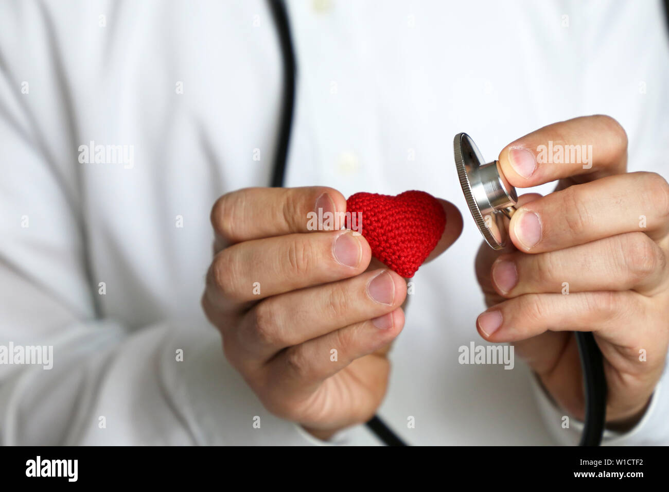 Doktor mit Stethoskop und Rot gestrickt Herz in der Hand. Konzept der Kardiologen, Herz Krankheiten, Diagnose, Blutdruck, medizinische Untersuchung Stockfoto