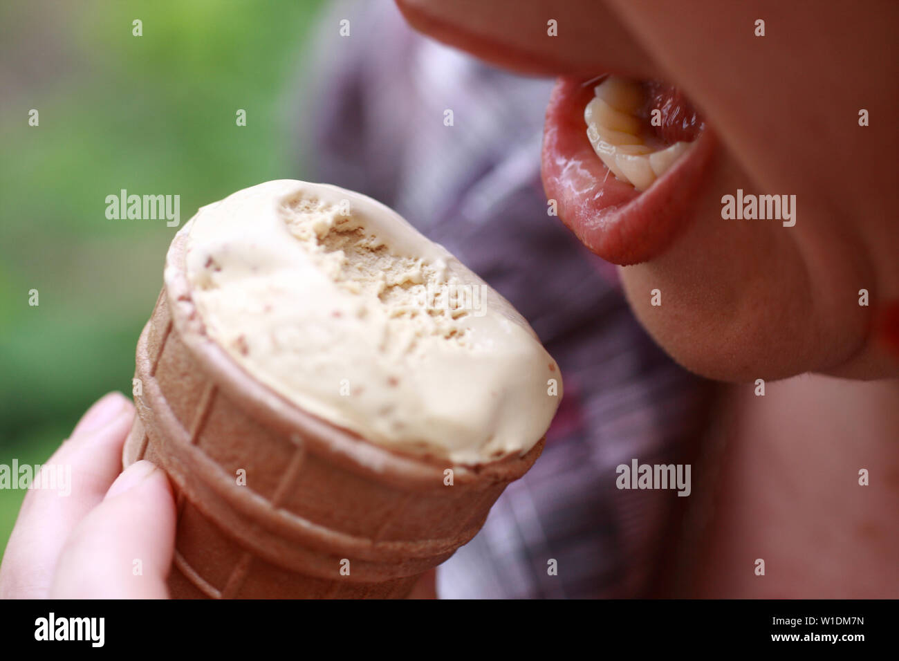 Das Mädchen öffnete den Mund, um einen Bissen von Eis in der Waffel Schale zu nehmen. Stockfoto