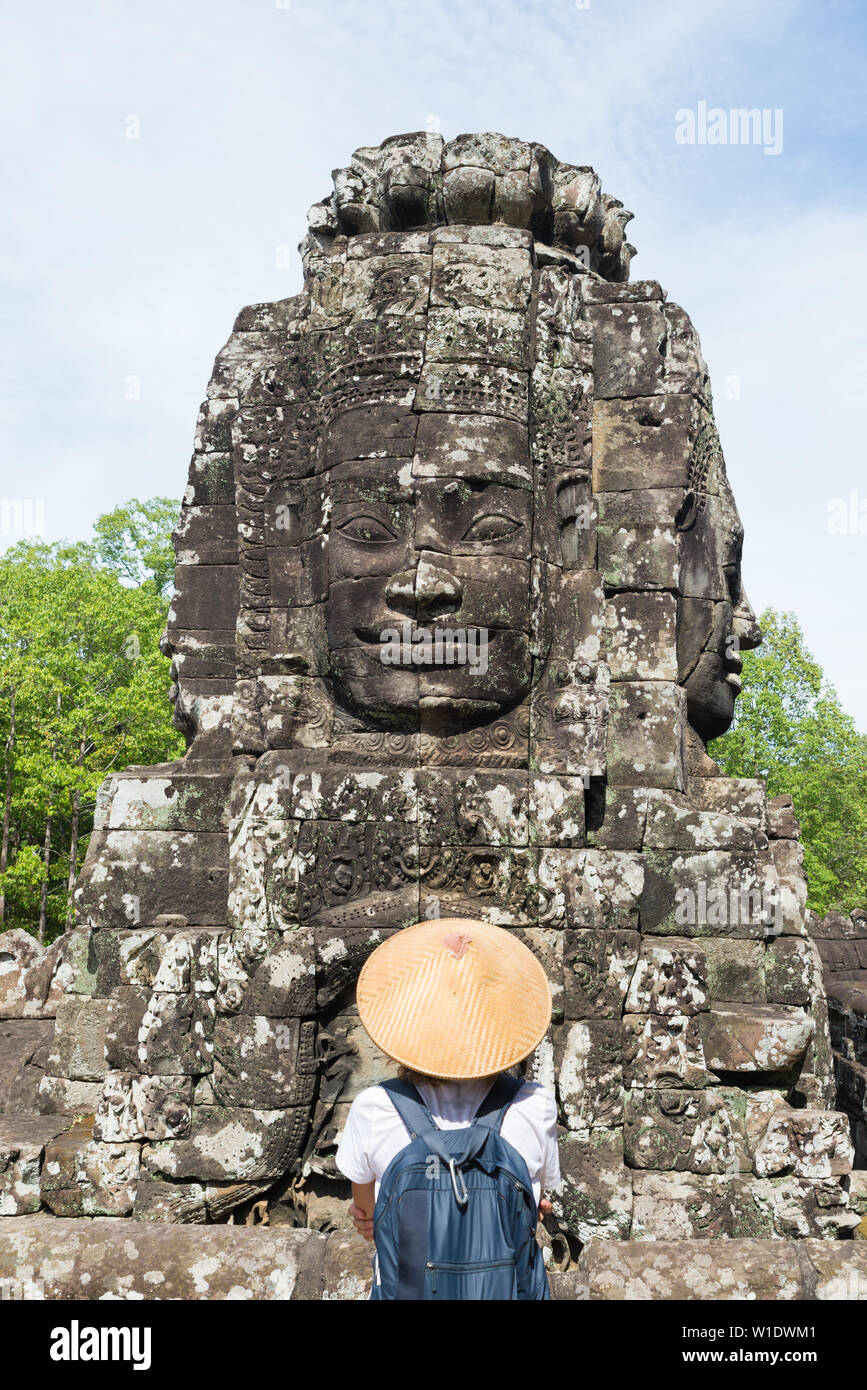 Frau in Bayon Tempel mit Blick auf Stein Gesichter, Angkor Thom, morgen Licht strahlend blauer Himmel. Buddhismus meditation Konzept, weltberühmten Reiseziel, Stockfoto