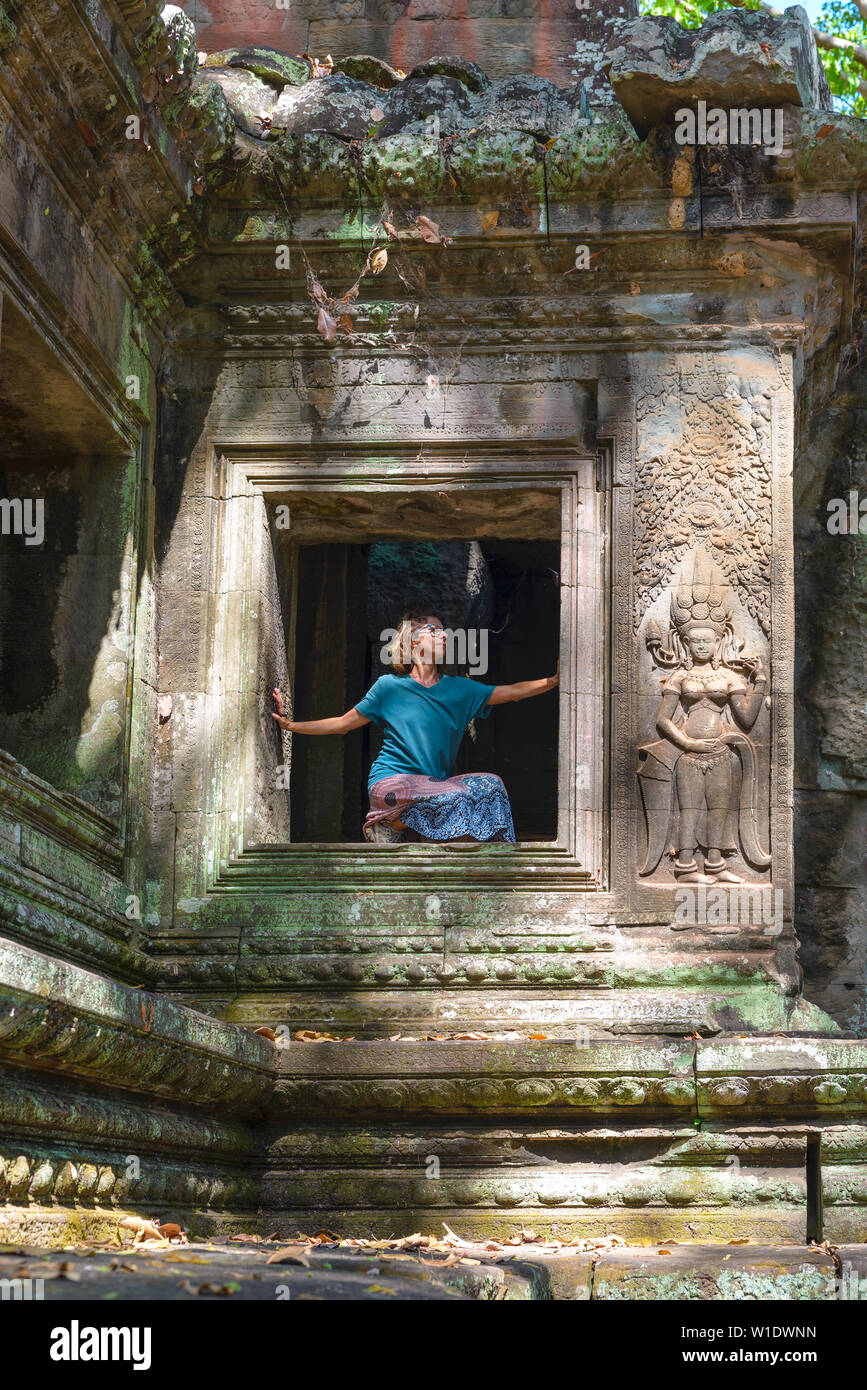 Eine Person in Angkor Wat Ruinen, Reiseziel Kambodscha. Frau in Yoga Position, Stretching Bein und hob den Arm, Profil ansehen, zwischen basreliefs ein Stockfoto