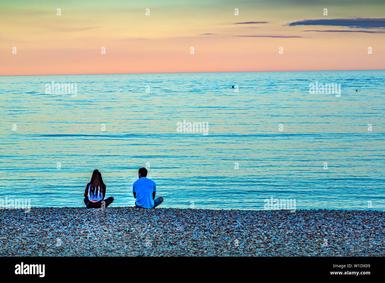 Ein junges Paar sitzen am Strand bei Sonnenuntergang in eine sehr romantische Szene. Stockfoto