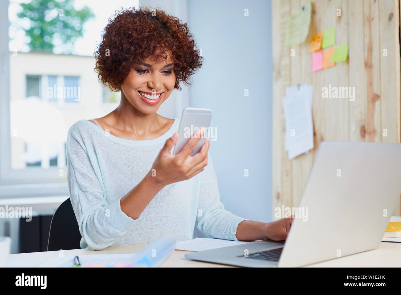 Glückliche junge Frau am Schreibtisch mit Ihrem Smartphone und Laptop Stockfoto