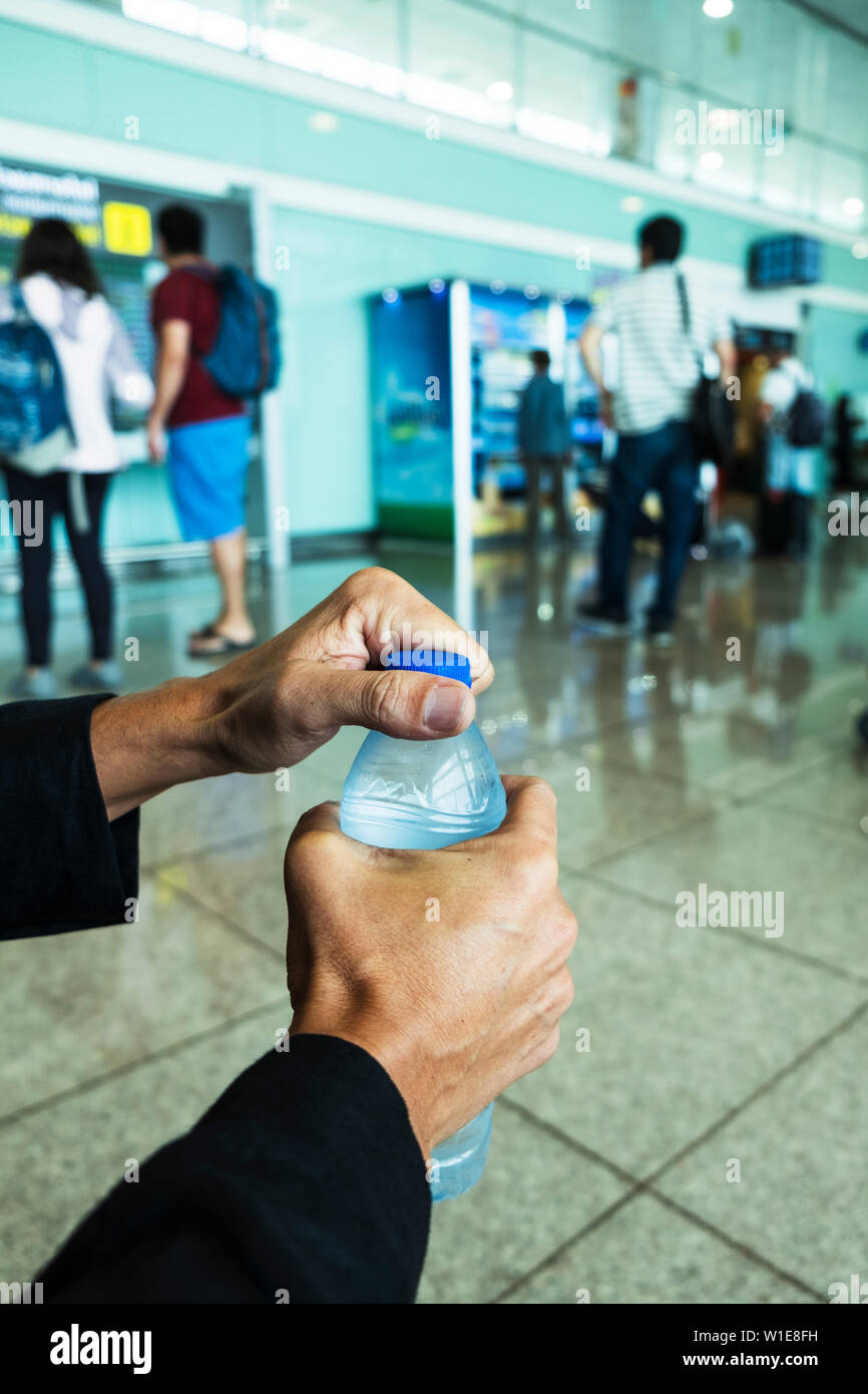 Nahaufnahme eines jungen kaukasischen Mann das Öffnen einer Flasche Wasser im Wartezimmer eines Bahnhof oder Busbahnhof oder Flughafen Stockfoto