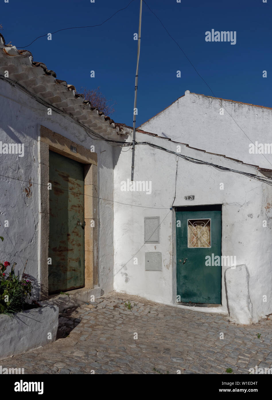 Zwei verblasst und Rost kleine Türen in weiß getünchten Gebäude in einer kleinen Straße Ecke in Estoi, in der Nähe des Palace. Estoi, Algarve, Portugal. Stockfoto