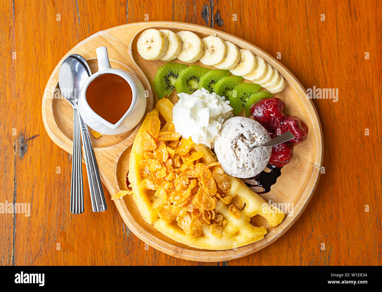 Süßes Wasser gießen auf die Waffeln mit Eis und Früchte wie Bananen, Kiwi und Erdbeeren in Holz- Platte auf dem Tisch. Stockfoto